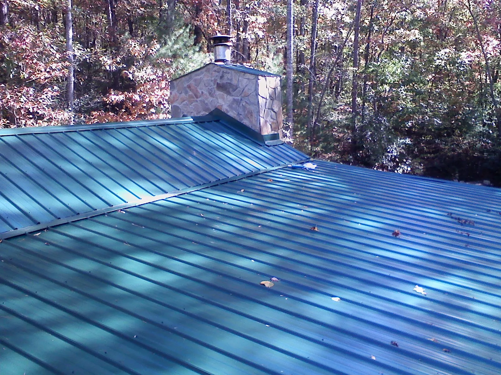 New green metal roof and stone chimney surrounded by autumn woods in Garden City